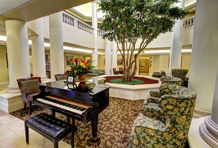 A luxurious lobby with a grand piano, surrounded by comfortable seating and a central plant display.