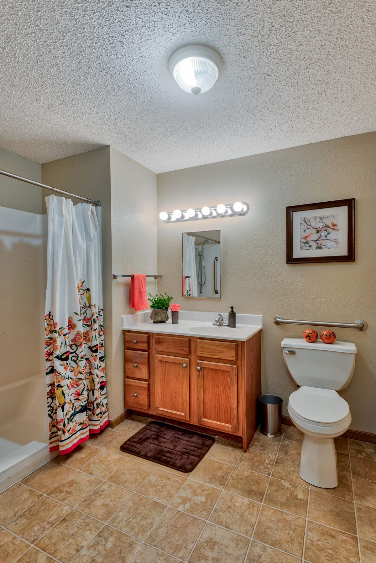 A well-lit bathroom with a shower, wooden vanity, and decorative elements.