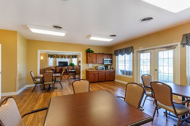 A spacious dining and kitchen area with wooden floors, tables, chairs, and large windows letting in natural light.