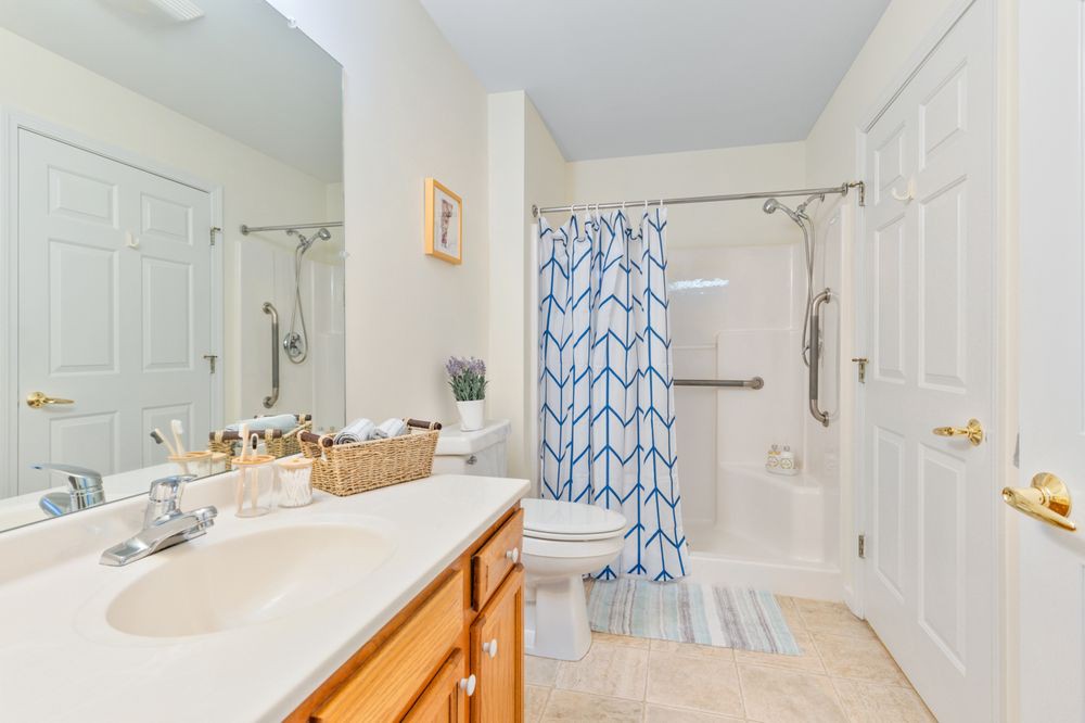 A clean and bright bathroom featuring a shower with a patterned curtain, a sink with a mirror, and neatly organized toiletries.