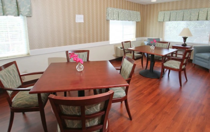 A cozy dining room with wooden tables and chairs, featuring a small vase with flowers on each table.