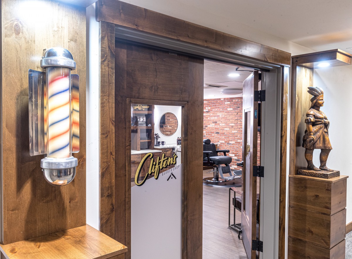 The entrance to a barbershop featuring a traditional barber pole and a view of the interior with exposed brick walls and salon chairs.