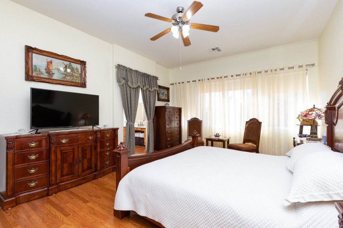 A classic bedroom with wooden furniture, a ceiling fan, and large windows with curtains.