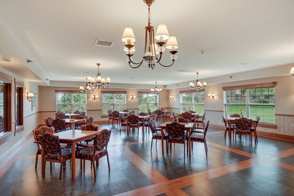 A spacious dining room with elegant chandeliers, wooden flooring, and neatly arranged tables and chairs.