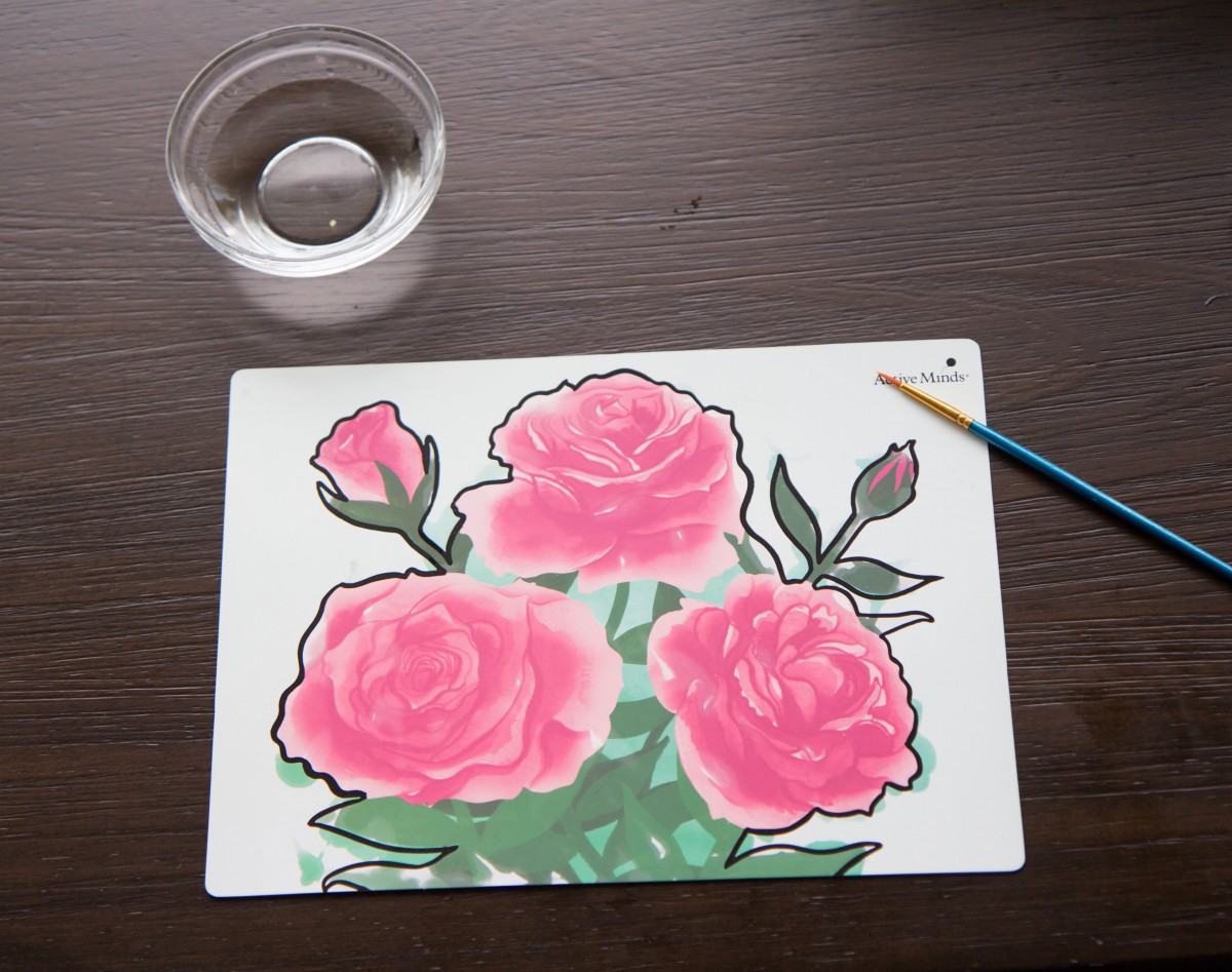 Watercolor painting of pink roses with a brush and water cup nearby.