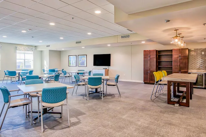 A modern conference room featuring tables and chairs, a television screen, and carpet flooring.