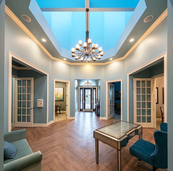 A luxurious hallway featuring a chandelier and skylight, with elegant furnishings and glass doors.