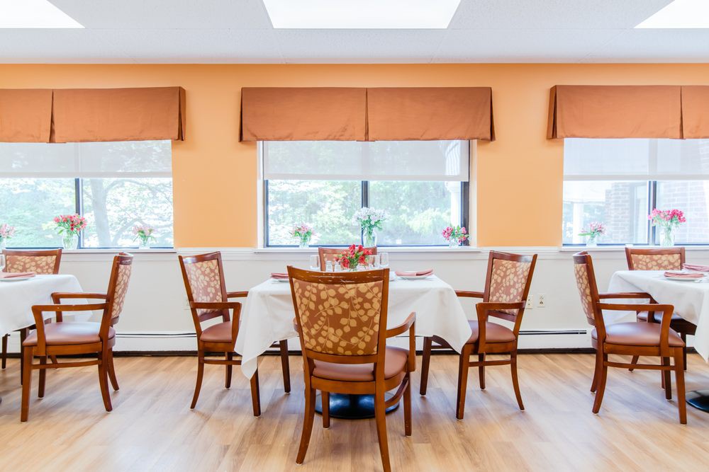 A bright dining room with a round table surrounded by six chairs, featuring orange walls and large windows.