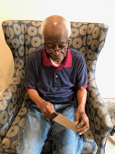 An elderly man sitting in an ornate chair, focused on a knife he's holding.