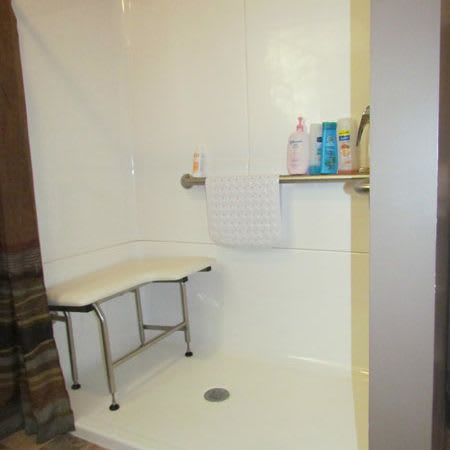 An accessible shower featuring a built-in bench and toiletries on a wall shelf.