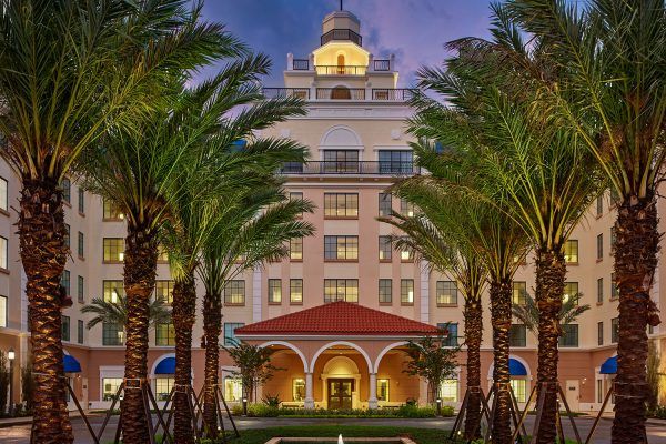 A luxurious hotel building beautifully lit in the evening, framed by tall palm trees.