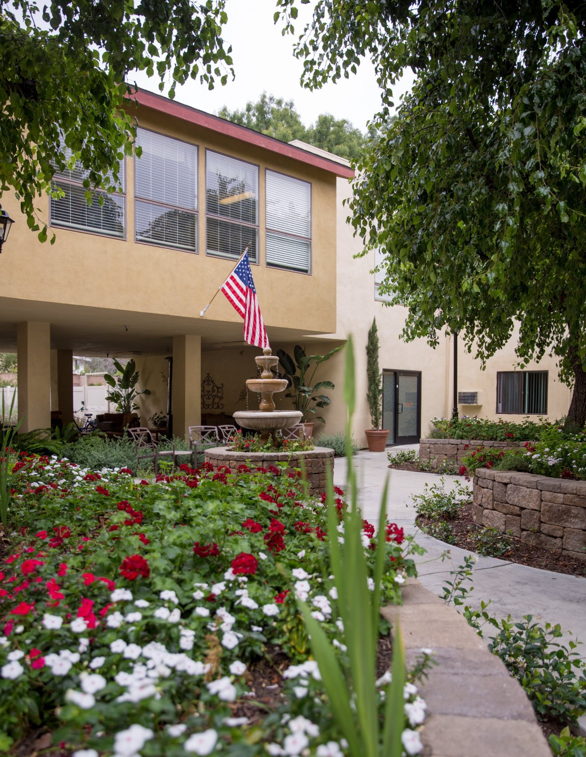 A well-maintained courtyard with colorful flowers and an American flag outside a building.