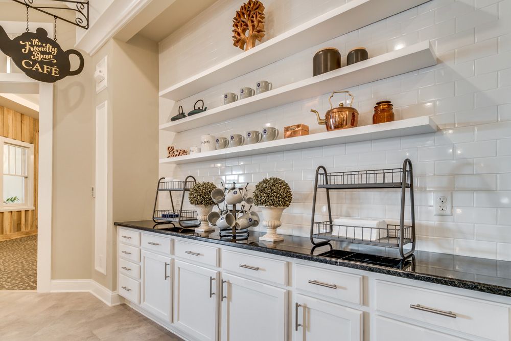 A beautifully organized kitchen with white cabinets, decorated shelves, and a black countertop displaying various kitchenware items.