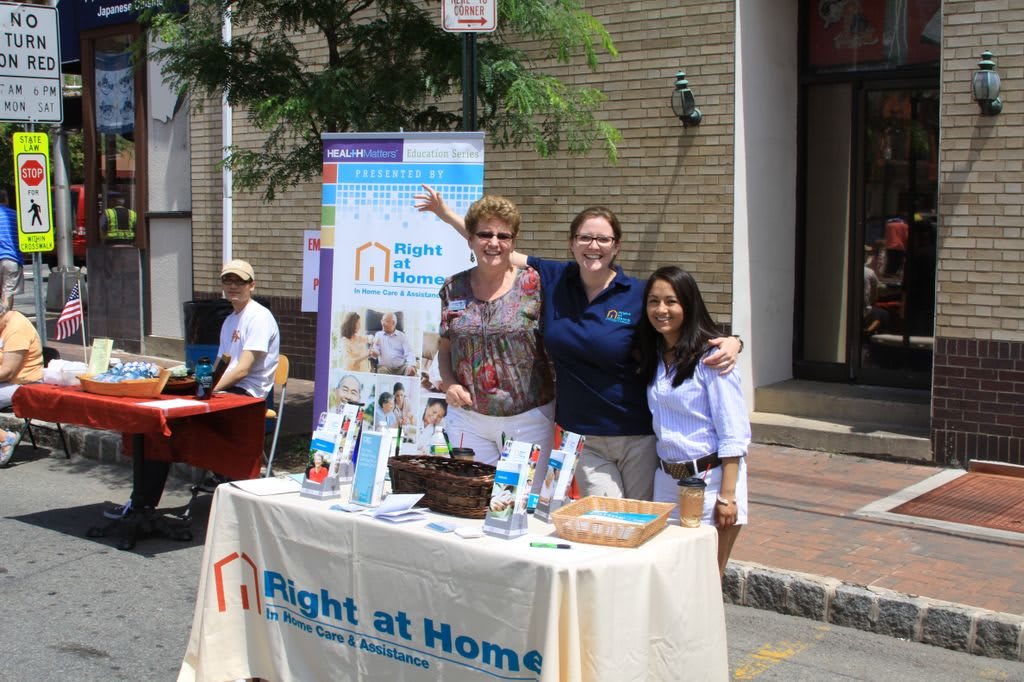 A group of people stand at an information booth for 'Right at Home' during a community event.