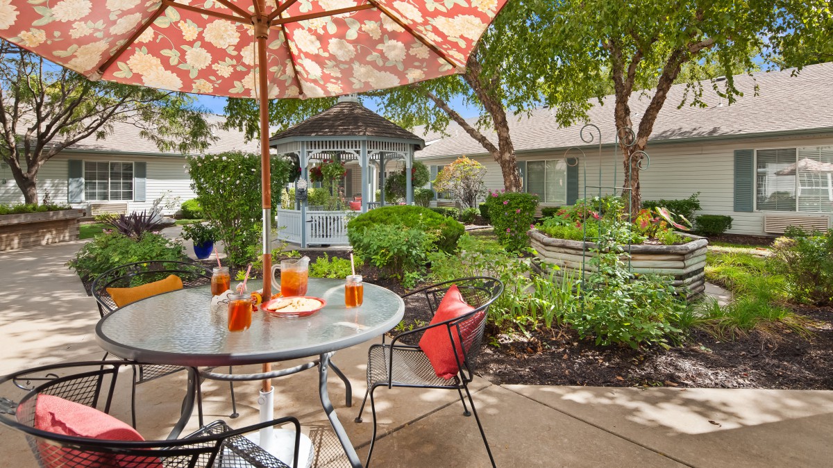 Charming outdoor patio with a garden view and refreshing drinks under a patterned umbrella.
