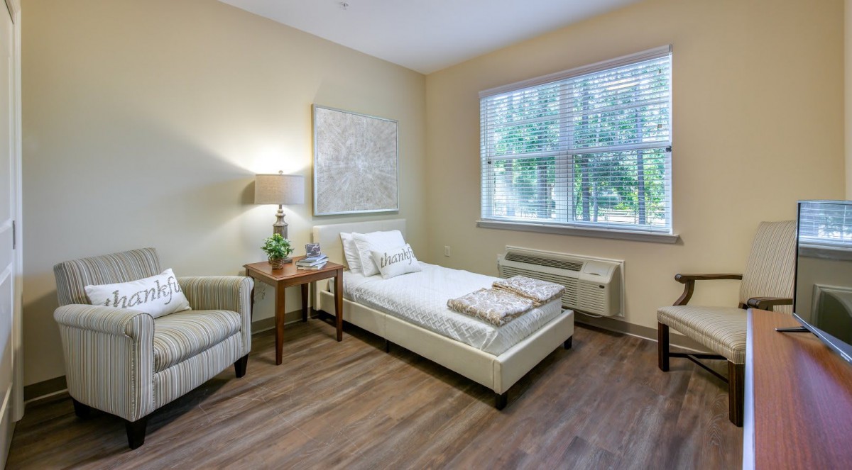 A cozy minimalist bedroom with a single bed, a lamp, and a window view.