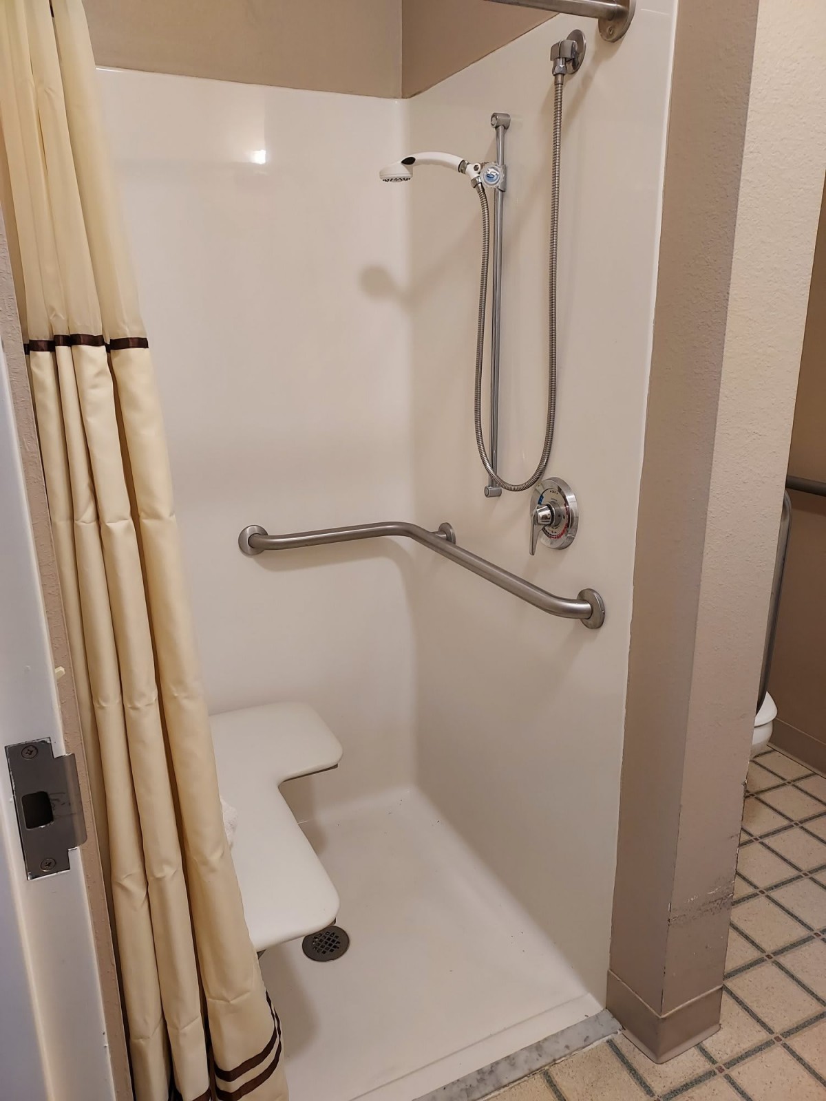 An accessible bathroom with a shower featuring grab bars and a seat.