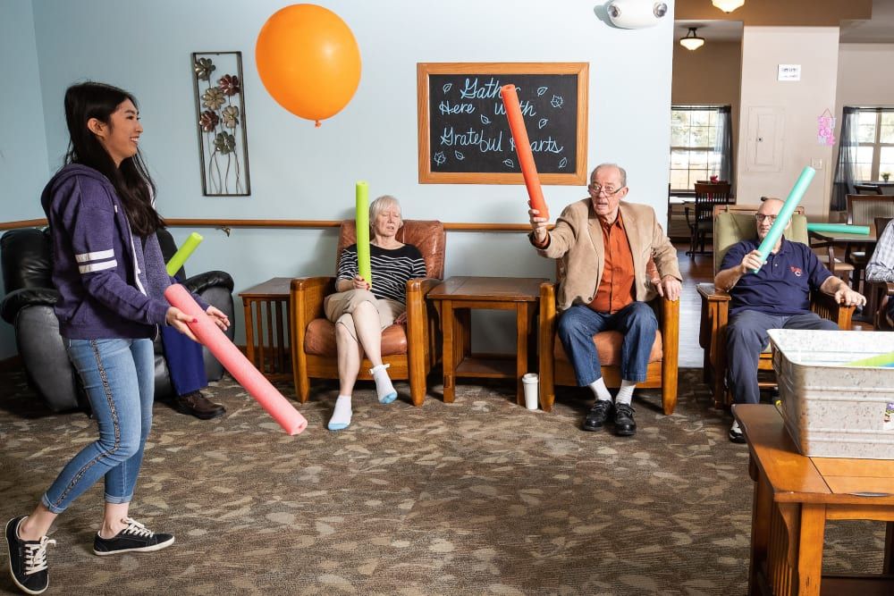 A group of seniors enjoying a fun activity with pool noodles and balloons indoors.