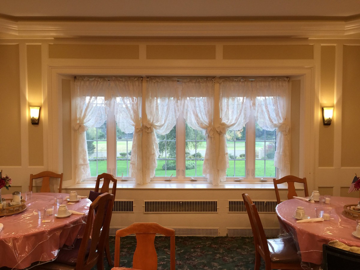 A cozy dining room with elegantly draped windows and neatly arranged tables and chairs.