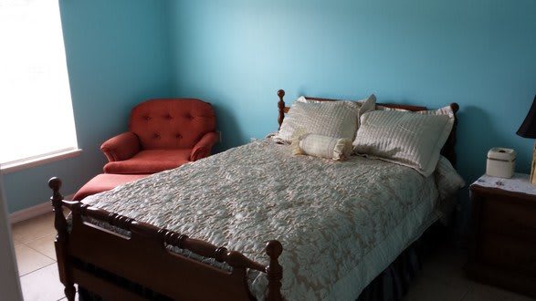 A cozy bedroom with a wooden bed frame, quilted bedding, and a red armchair against blue walls.