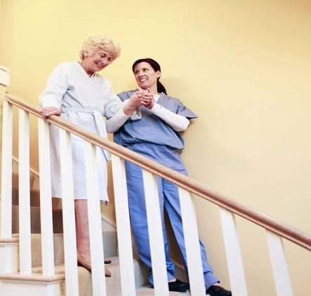 A nurse assists an elderly woman down the stairs, highlighting support and care.