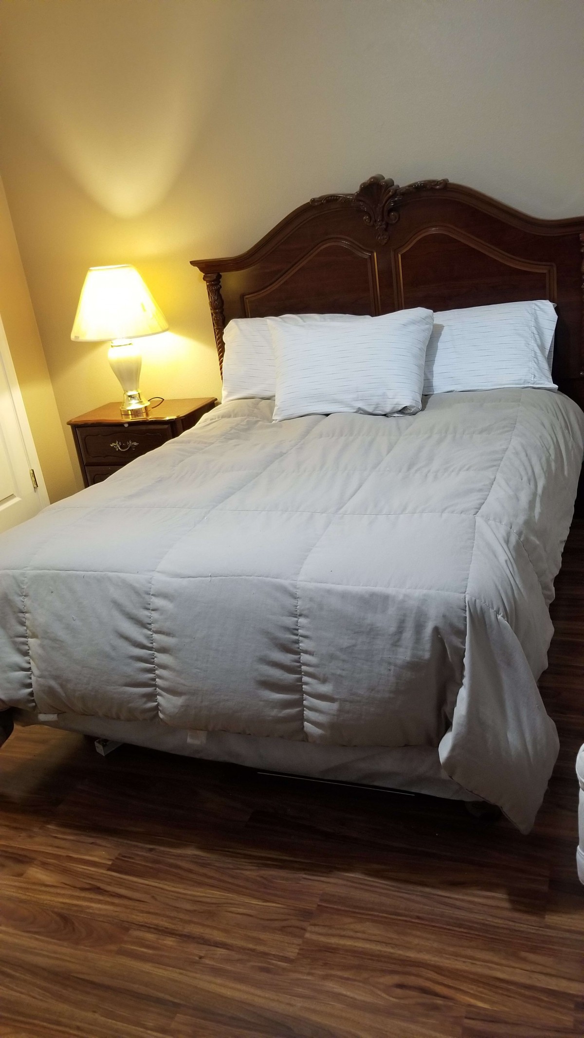 A neatly made bed in a cozy bedroom with a lamp on the nightstand.