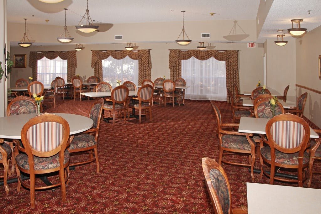 An empty dining room with arranged tables and chairs, featuring a patterned carpet and elegant curtains.