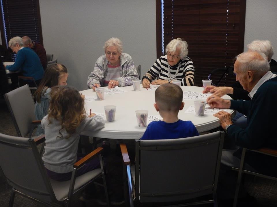 Children and seniors sitting together around a table, engaging in an activity.