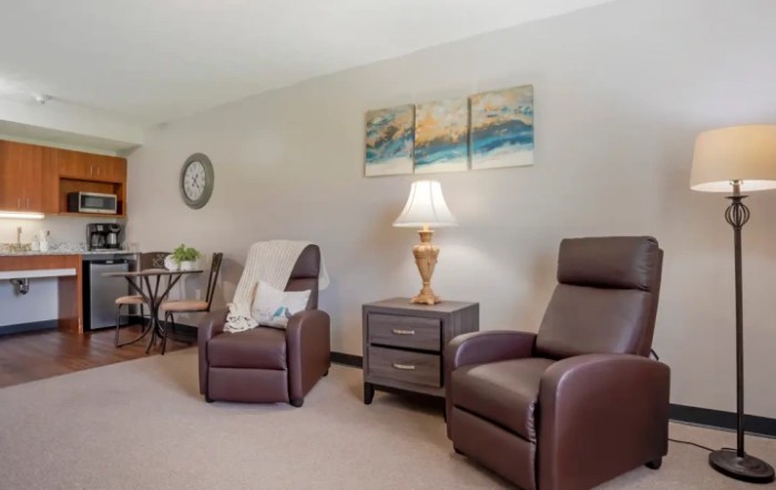 A cozy living room with brown armchairs, a side table with a lamp, and wall art.