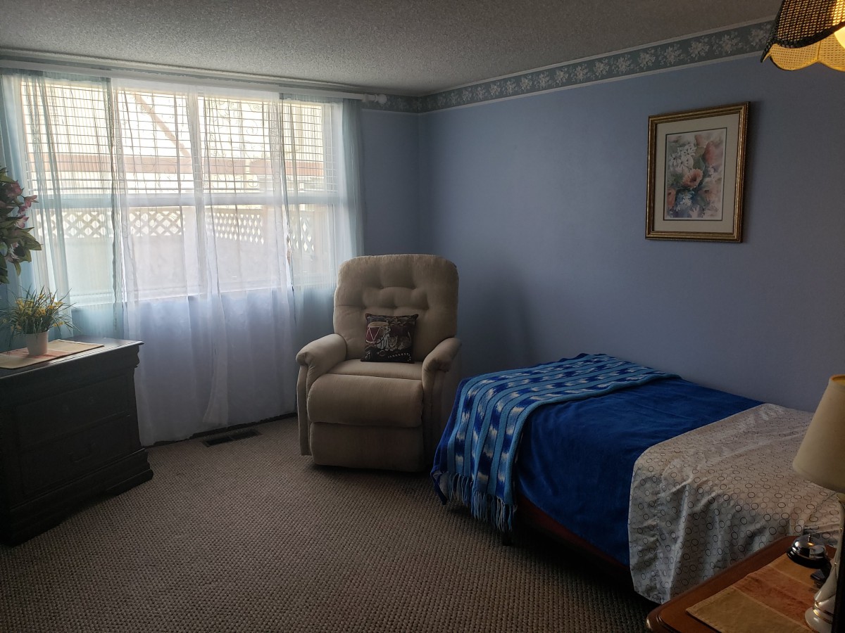 A cozy bedroom with a bed, armchair, and window with white curtains.