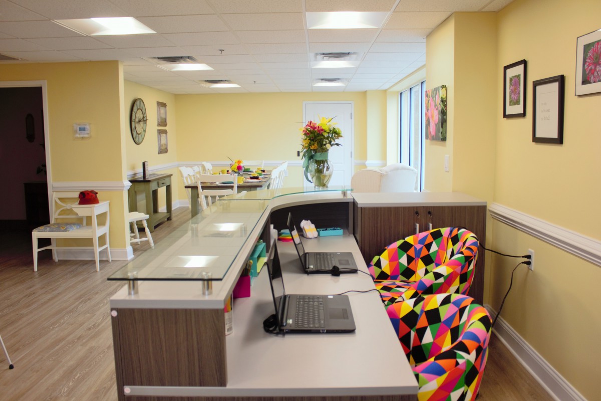 A welcoming office reception area with a desk, laptop, colorful chair, and flowers.