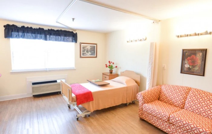 A clean and well-organized hospital room with a bed, chair, and natural lighting.