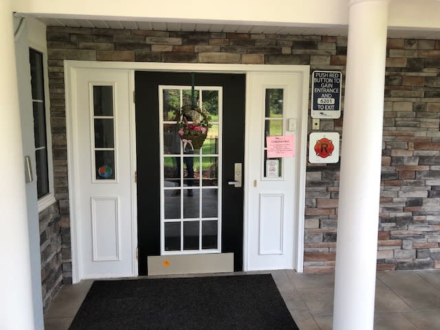 A building entrance with glass double doors, framed in white and set against a brick wall.