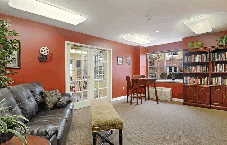 A cozy living room with red walls, featuring a comfortable sofa, a small table with chairs by the window, and a decorative wall piece.