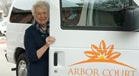 An elderly woman standing next to a van with the logo 'Arbor'.