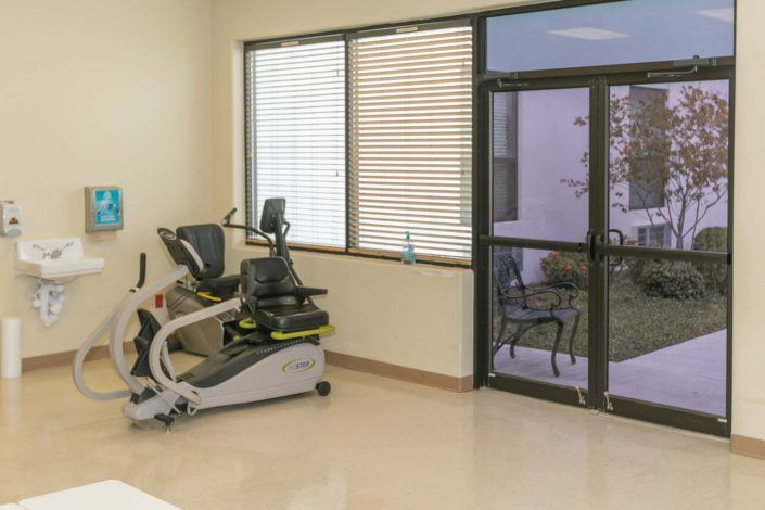 A well-lit gym room with a stationary bike by the window.