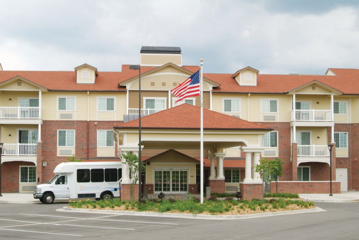 A hotel building with an American flag and a shuttle bus parked in front.