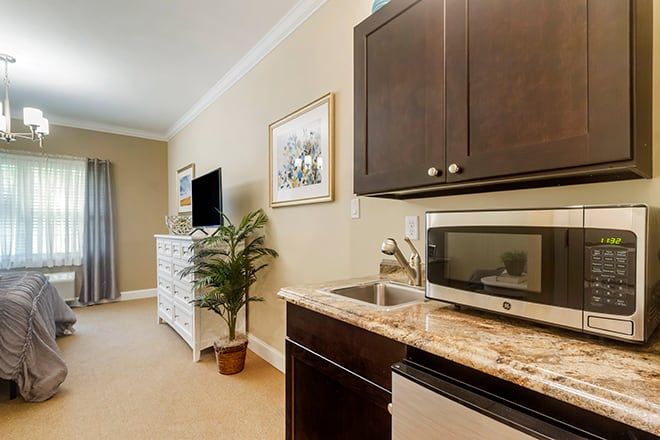 A cozy kitchenette with dark cabinets and a microwave, leading into a living area with a television.