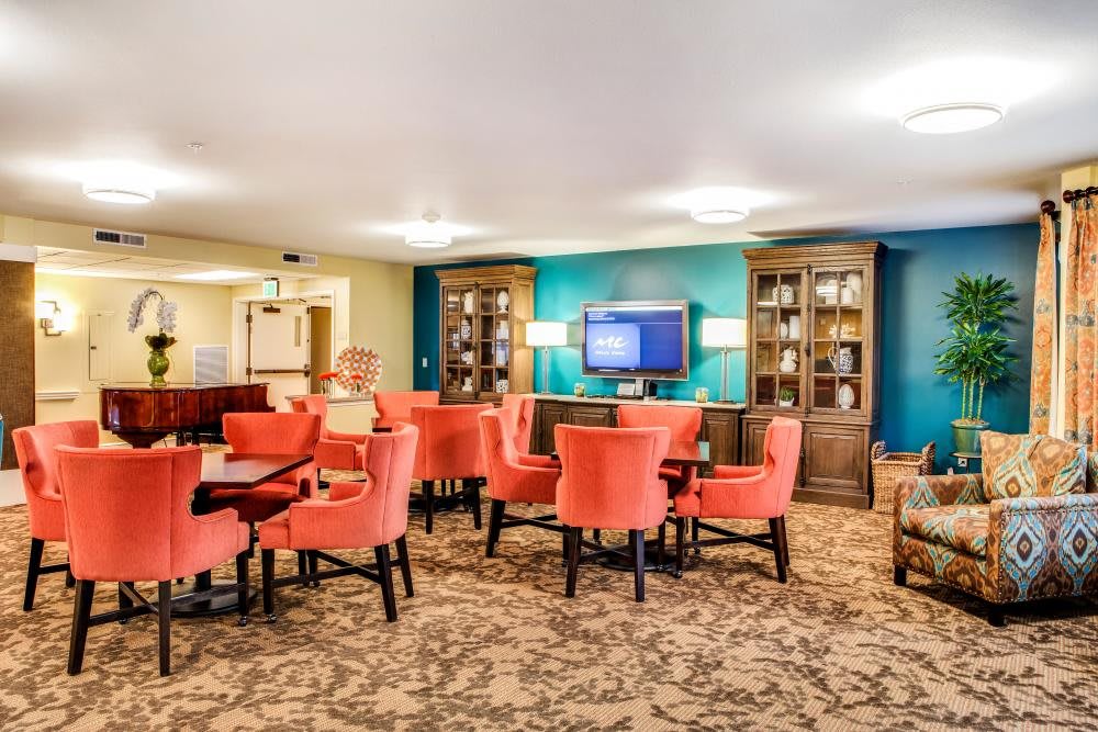 A cozy lounge area with coral chairs, patterned carpet, bookshelves, and a central television.