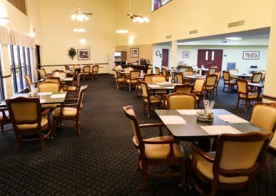 An empty dining area with neatly arranged tables and chairs, carpeted flooring, and soft lighting.