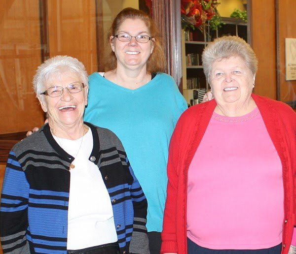 Three women posing together indoors, all smiling at the camera.