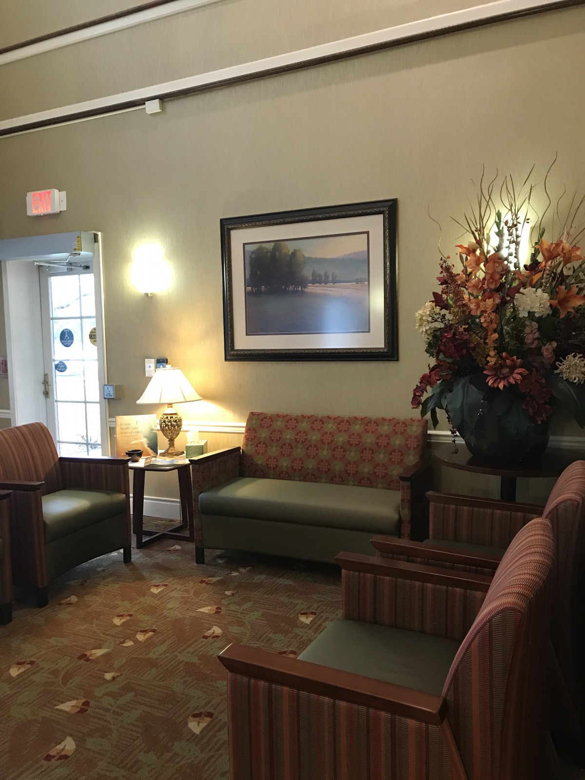 A cozy waiting room with comfortable seating, a decorative painting, and a floral arrangement.