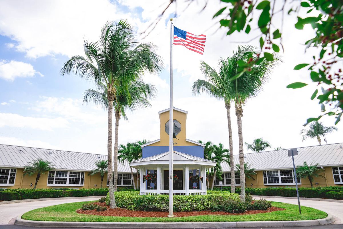 A building entrance surrounded by palm trees with an American flag on a flagpole.