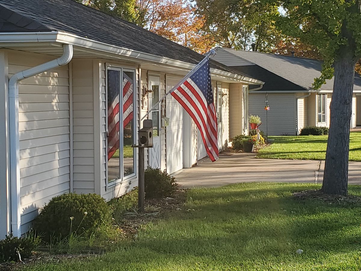 A suburban house with an American flag displayed, surrounded by autumn trees.