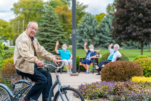 A cheerful man enjoying a bike ride in the park, greeted by friendly seniors sitting nearby.