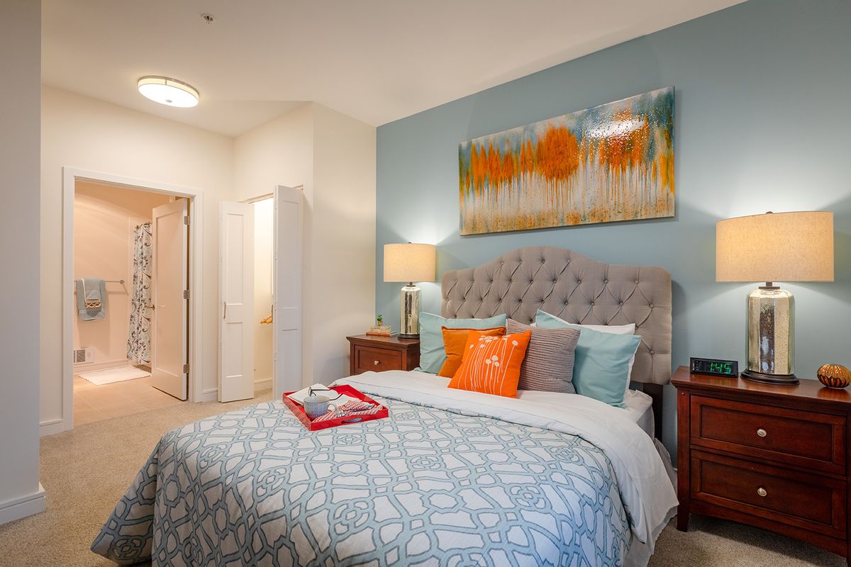 A cozy bedroom with a stylish bed adorned with colorful pillows and modern artwork on the wall.