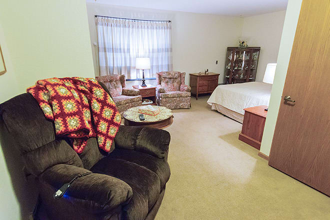 A cozy living room with a bed, armchairs, and a decorative quilt.
