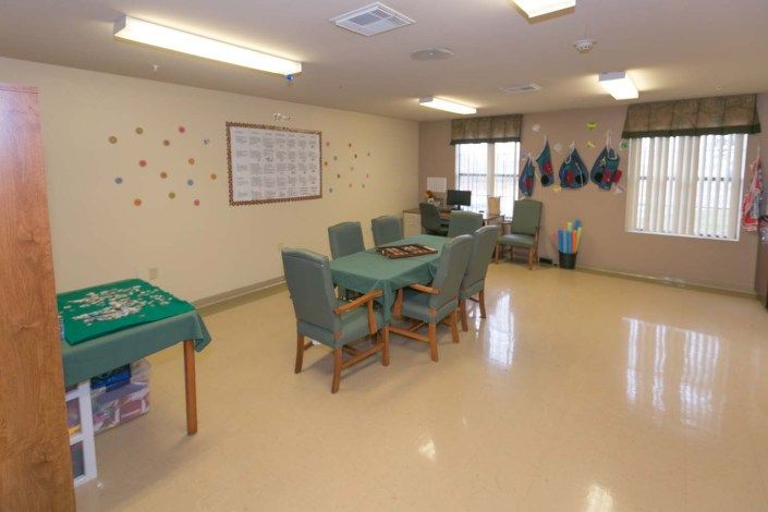 An activity room with tables and chairs, decorated walls, and bright lighting.