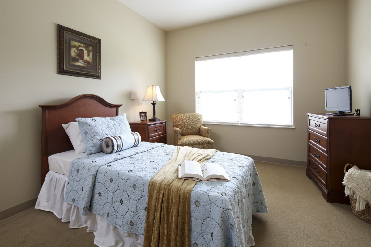 A cozy bedroom with a single bed, elegant furnishings, and natural light from a large window.