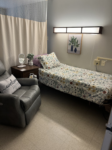 A cozy and well-lit hospital room featuring a patient bed, recliner chair, and decorative elements for comfort.